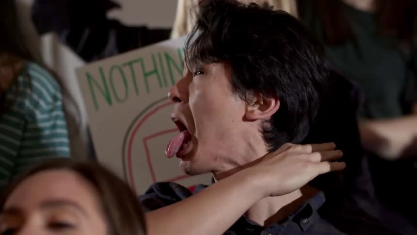A crowd of teens cheer at an event while one asian teen yells and pretends to cut his throat with his hand