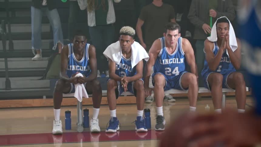 Team members sit on a bench and yell as a crowd stands behind them