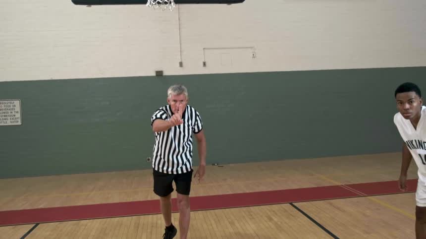 A referee tosses a basketball to a black player who is about to make a free throw