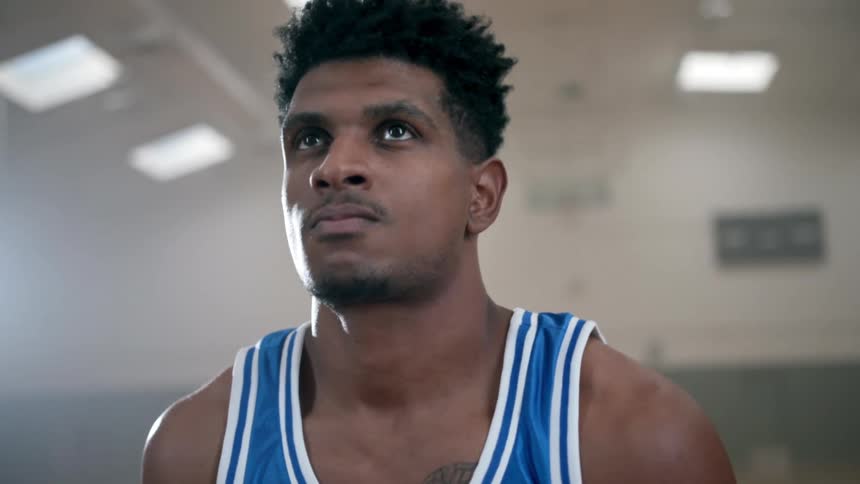 Determined black basketball player with a blue jersey shoots a basketball in the basketball court