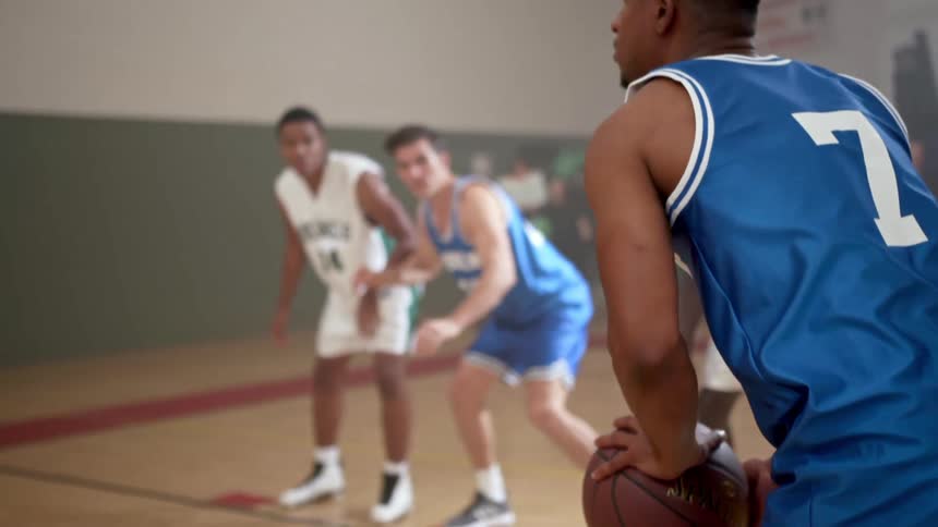 A teenager takes a free throw in a basketball game as other players watch and people cheer on the sidelines