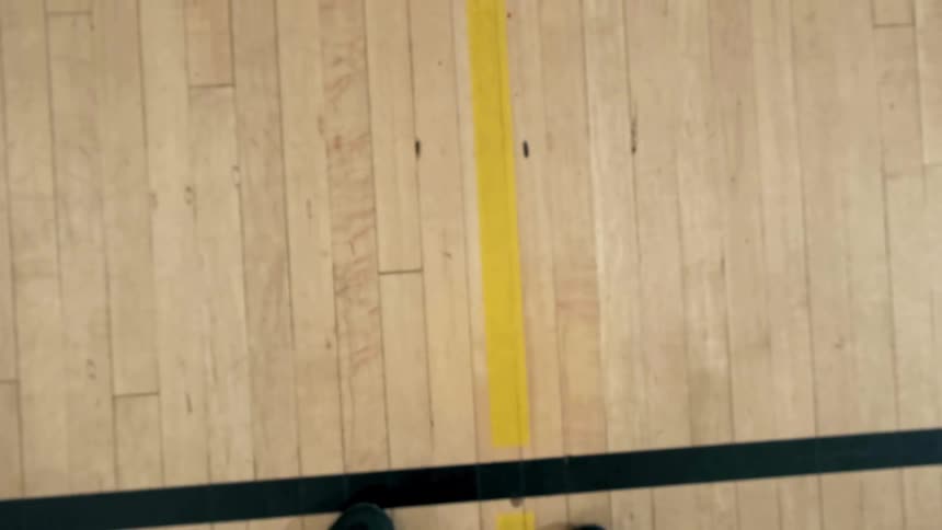 Person dribbles basketball on wooden court near lines