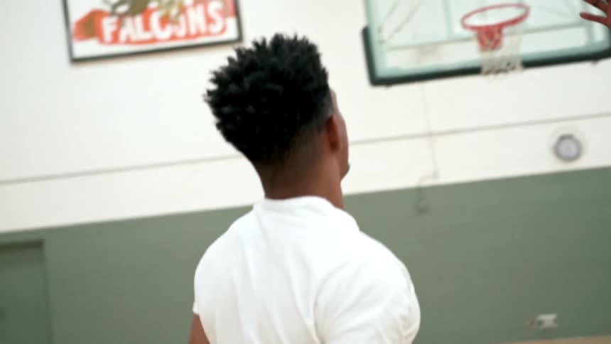 Black basketball player with a white t shirt shoots a basketball in a basketball court