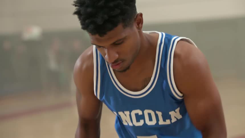 Black man wearing a jersey bounces a basketball then shoots it