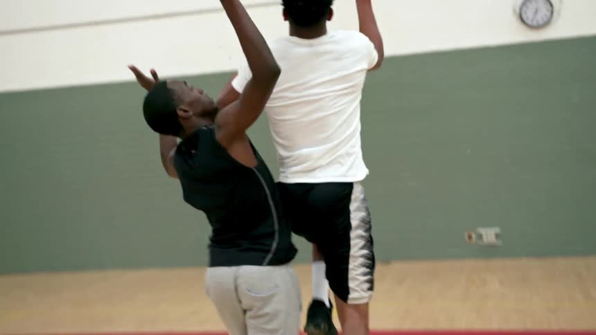 A teenager dribbles a basketball and shoots as another guards him