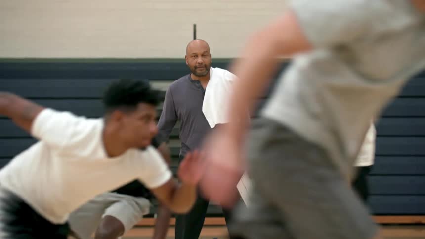 A basketball coach watches his team players as they perform sprinting drills inside a gymnasium