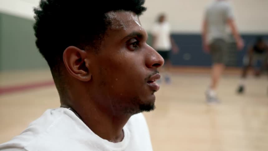 Black man sits on the gym floor as a caucasian man walks behind him