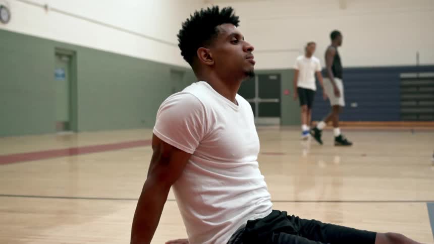 Man sits on the floor in a gym while other men walk nearby