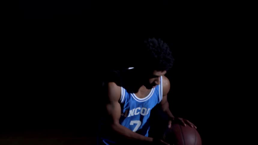 A man bounces the basketball in the pitch black room