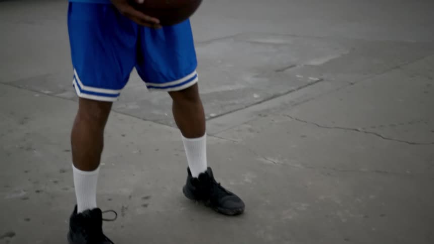 A young black man dribbles and basketball and then stops and holds it and takes a deep breath