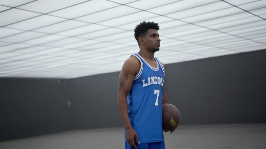 A young black man stands inside holding a basketball