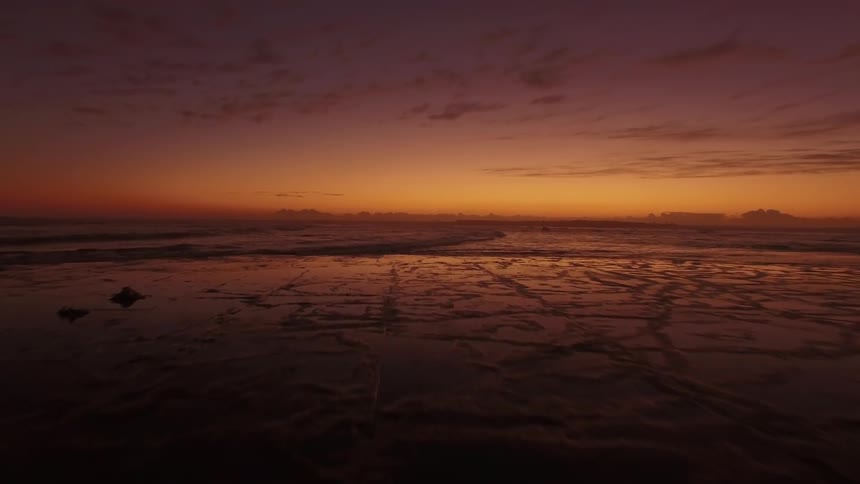 a colorful dawn breaks over patterned shoreline with birds