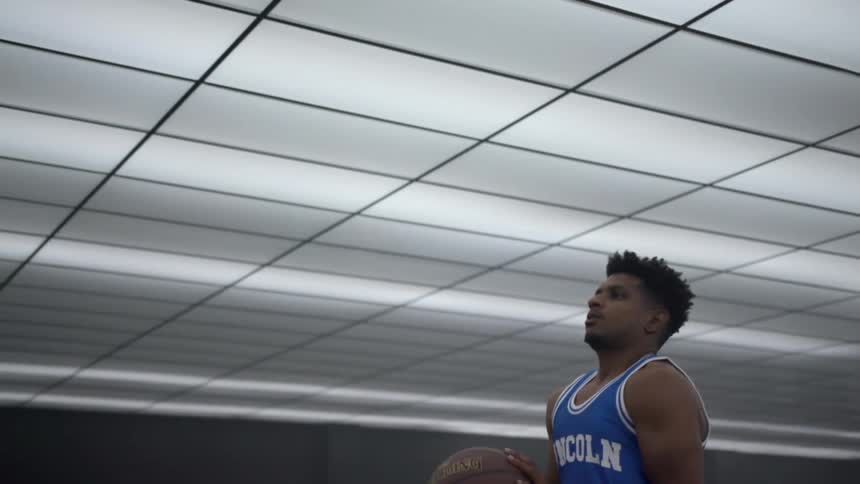 Man wearing sports jersey and holding basketball breathes deeply as fluorescent ceiling lights are turned on