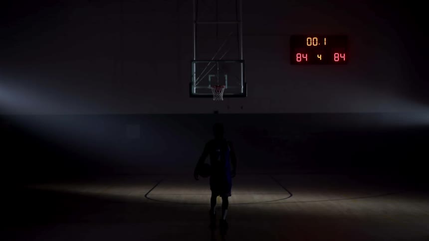 A basketball player holding a basketball slowly approaching the goal in a dark basketball court