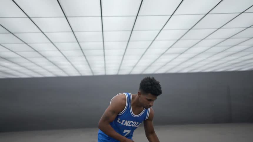 A basketball player takes a deep breath and dribbles a basketball in a concrete room