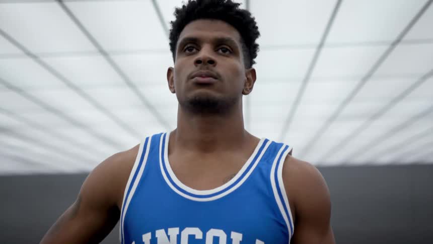 A basketball player poses with a ball under his arm in a gym