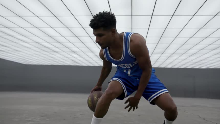 A teenager dribbles a basketball between his legs in a large open room