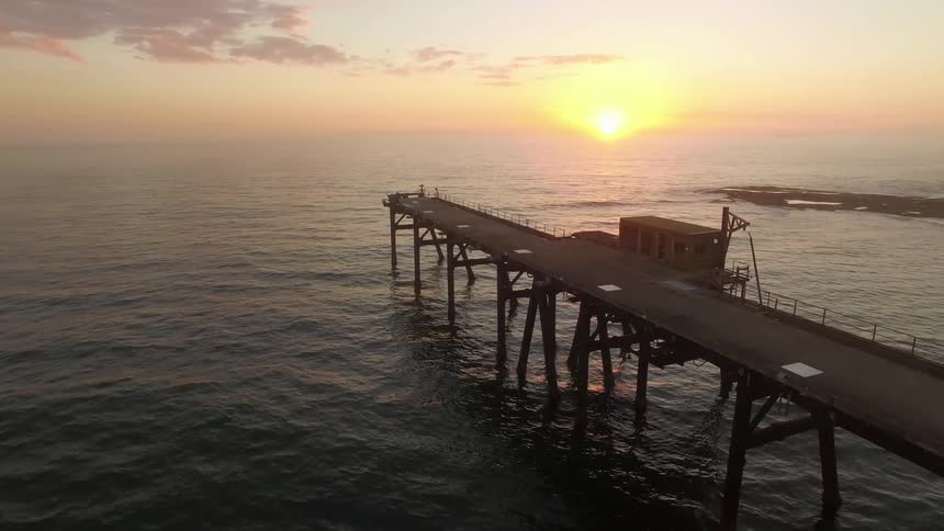 A sun is setting in the distance from a pier