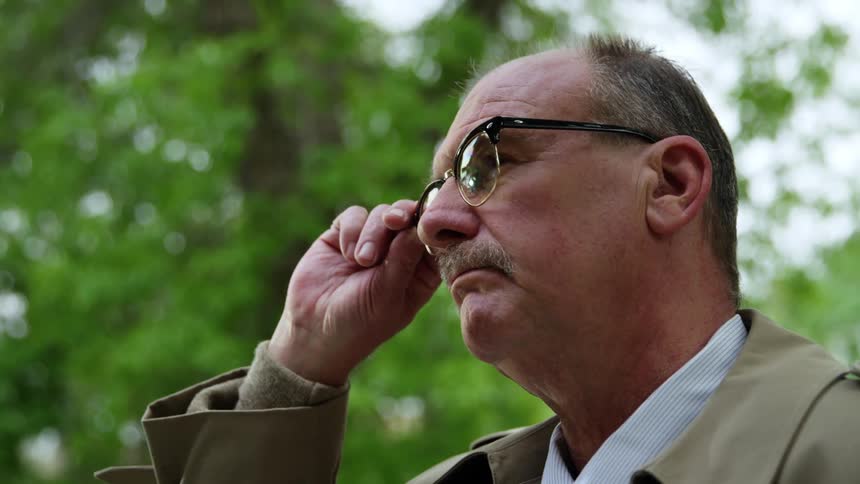 Man stands near the trees and adjusts his glasses then walks away