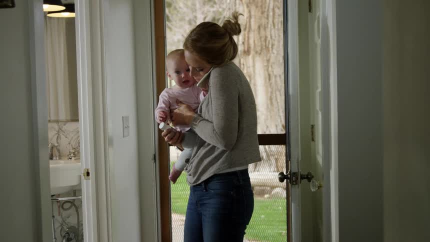 A mother holds her baby and talks on her cellphone at home