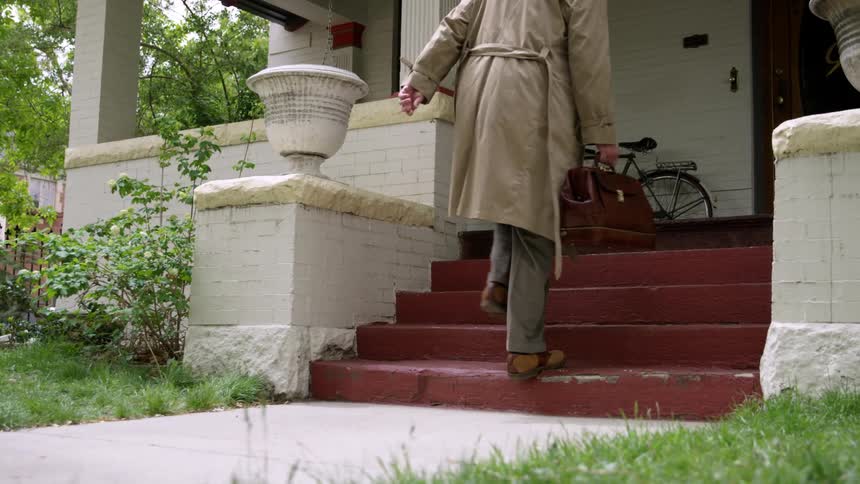 A man carries a leather bag to the front porch of a home