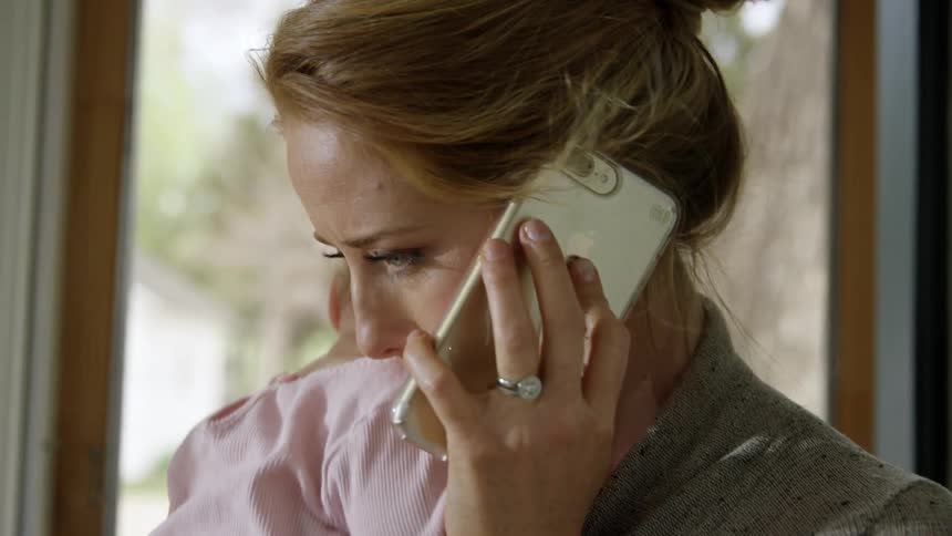 Blonde mother holding her baby talks on a smartphone with a concern