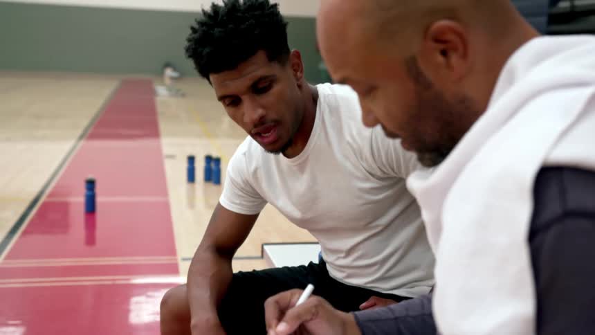 An athlete and coat sit on a bench and chat in a gym