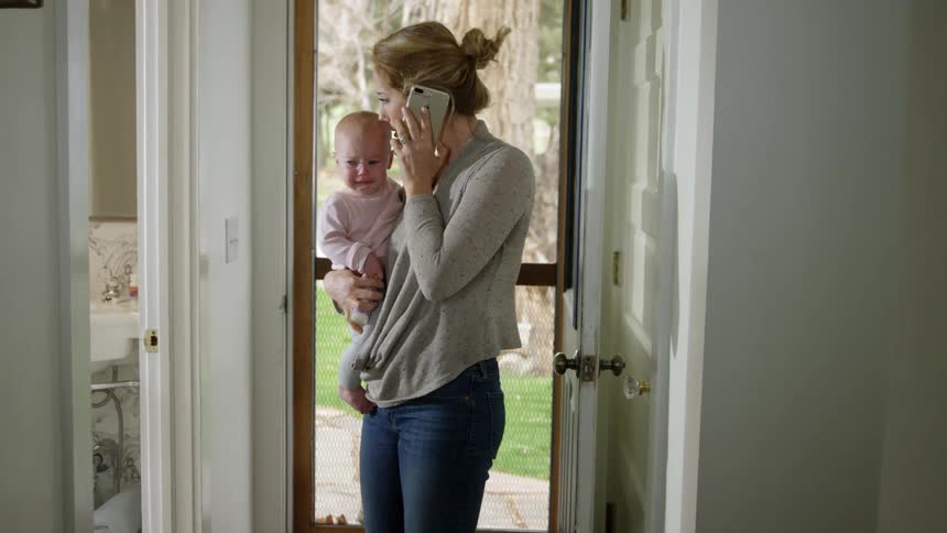 A mother holds and rocks her crying baby as she talks on her cell phone