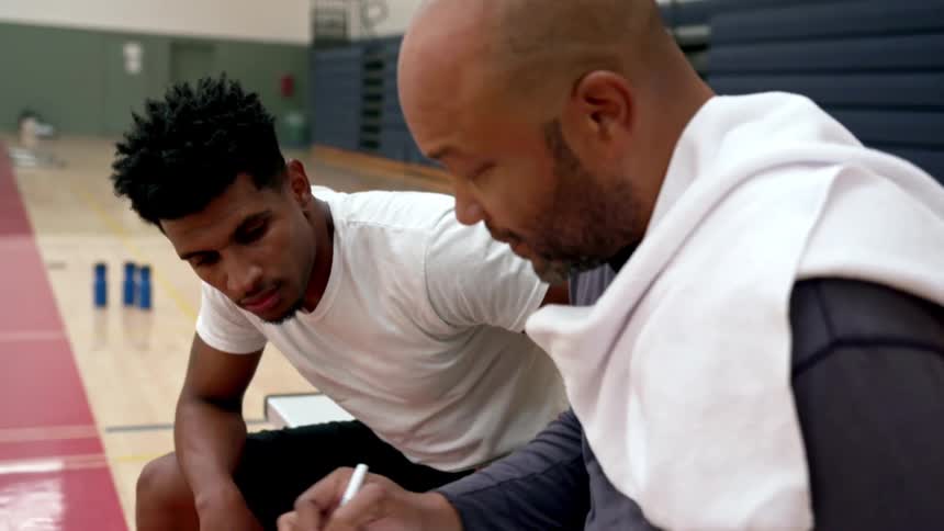 Coach sits with player on a bench in a basketball court