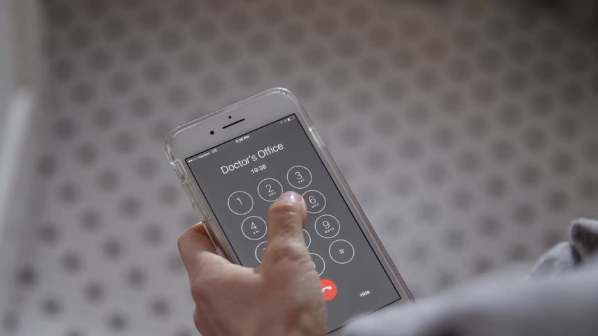 A woman holding a baby calls a doctors office on her cell phone