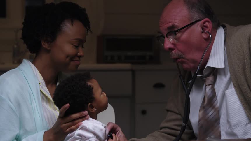 A woman holds her baby in her lap as a doctor listens to her heart