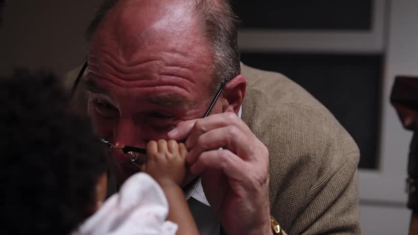 A doctor laughs as he tries to examine a baby at her home and she pulls his glasses off