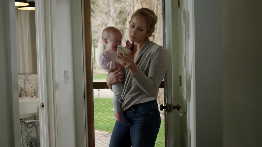 Mother holds crying son in her arms while calling on smartphone from home