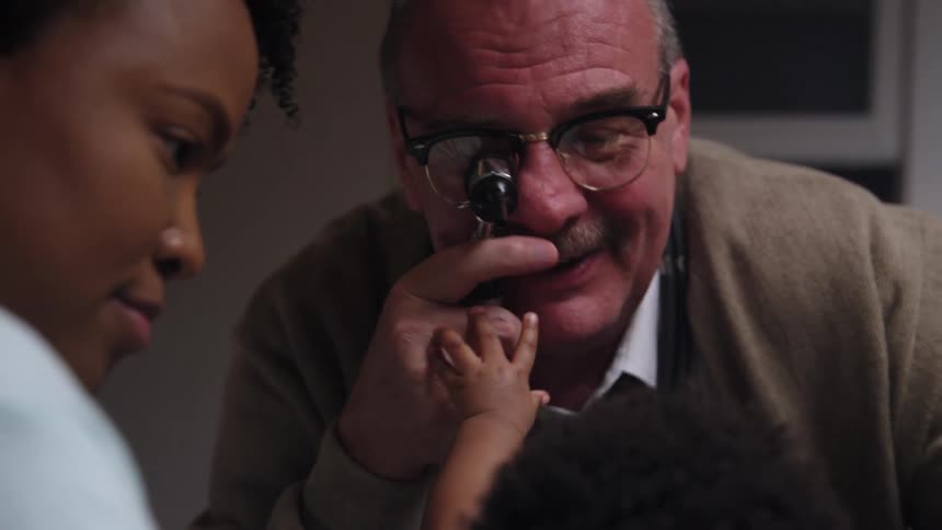 A male doctor holds a device to his eye trying to examine an infant