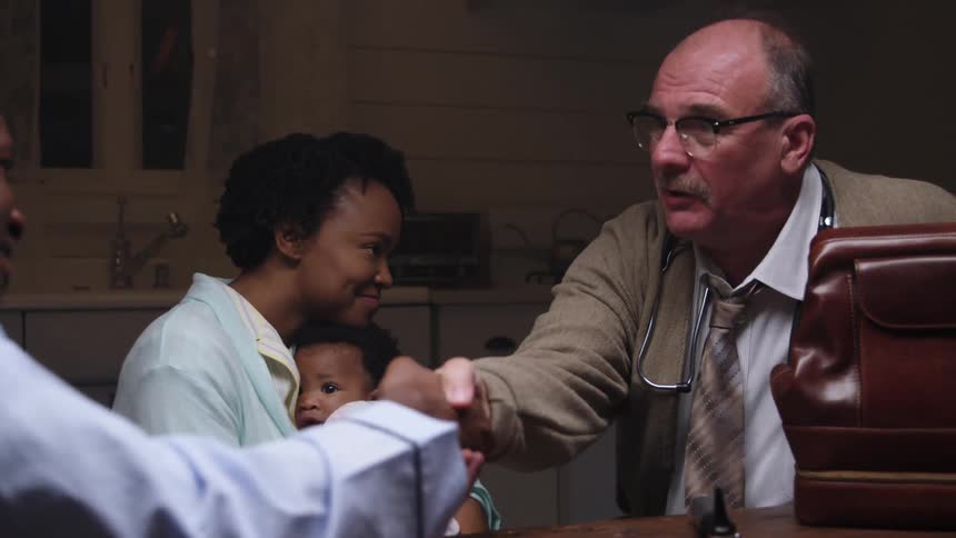 A doctor shakes a mans hand as he sits in their kitchen making a house call