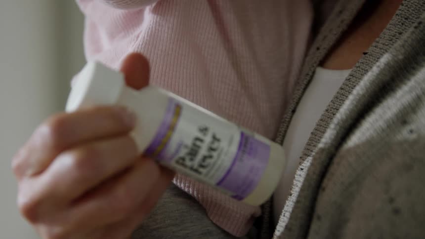 A mother holds her baby as she reads directions on a bottle of medicine