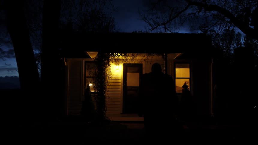 A man is walking into a house at night