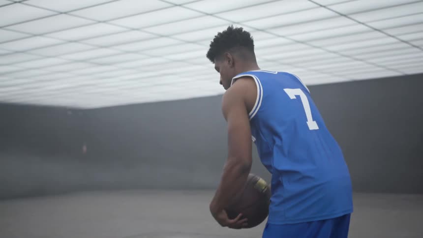 A basketball player dribbles a ball and prepares to shoot in an empty low ceilinged training facility