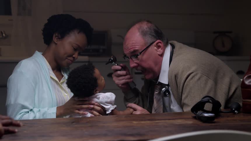 Person taps fingers as woman holds daughter while doctor examines her