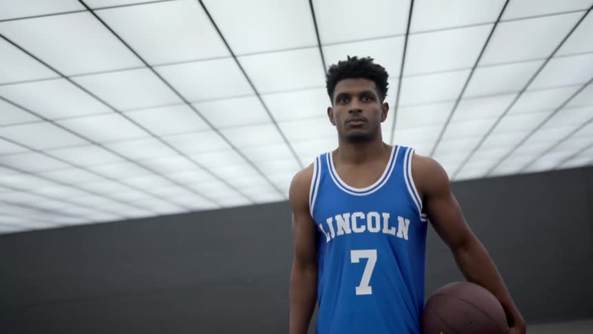 A black teenager stands and holds a basketball