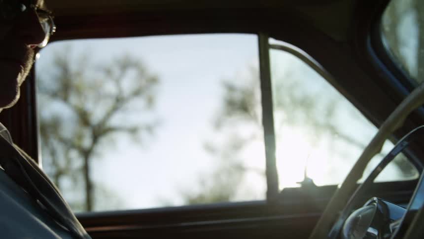 A man with a shirt and tie and glasses sitting and closing the door of a vehicle