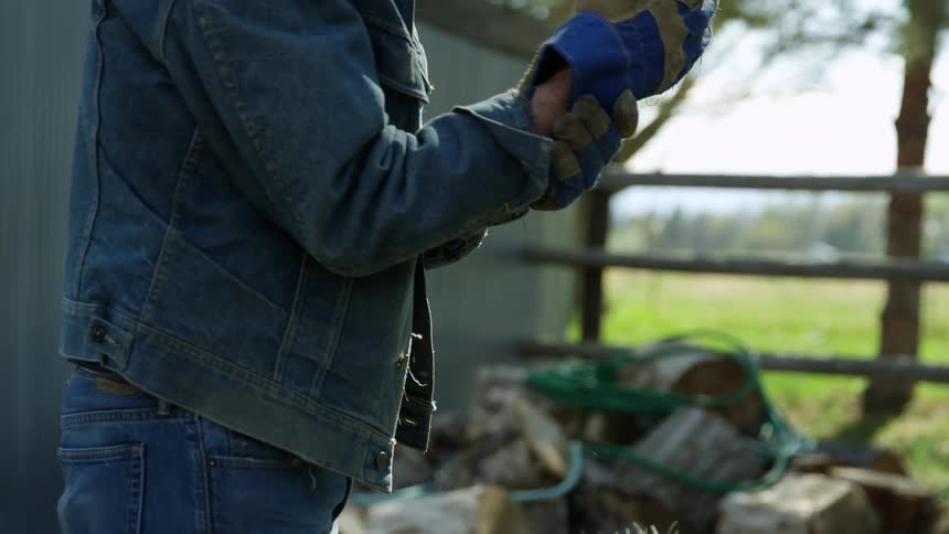 An elderly man lifts a hay bale and then rubs his wrist