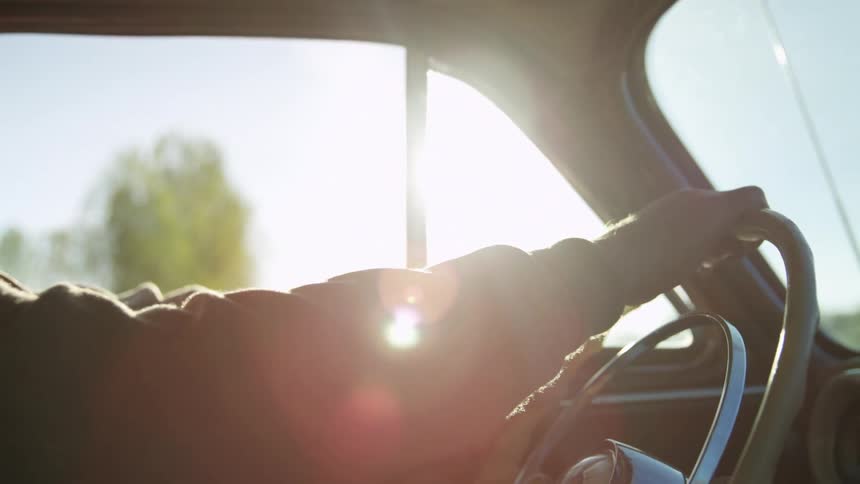 A man smiles as he drives a vintage car on a bright sunny day