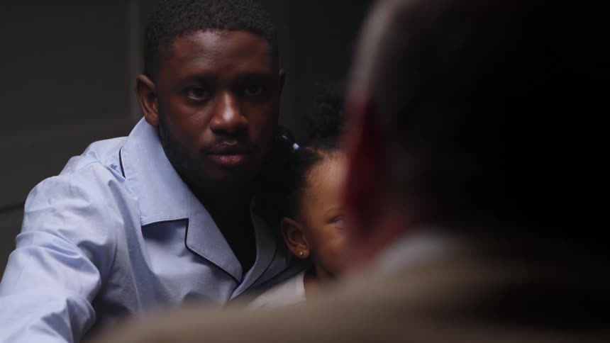 A black man with his daughter on his lap reaches over and shakes a mans hand