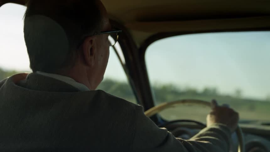Elderly man with glasses drives a classic car in the countryside