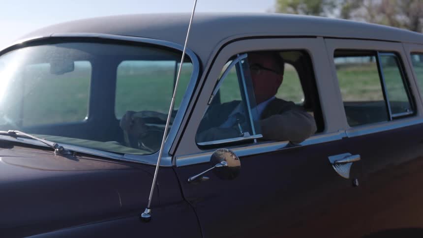 A man drives a vintage car in a rural area