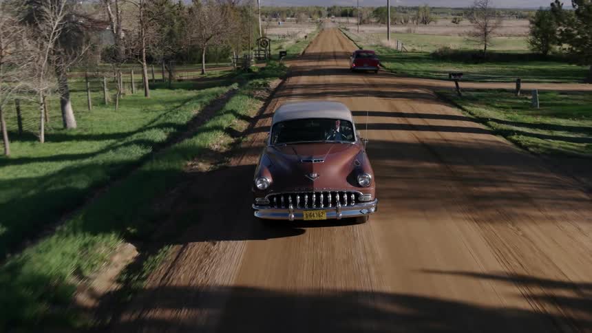 Classic car driving on a dirt road in the country side