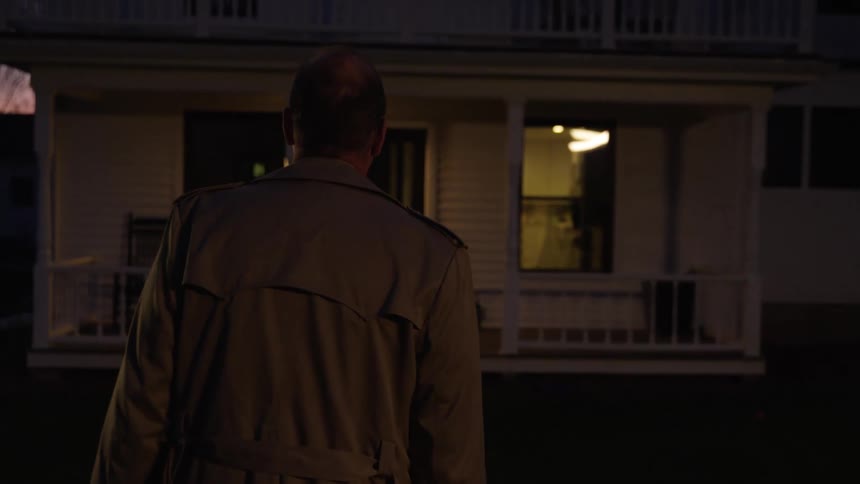 Man wearing an overcoat approaches a home entrance at sunset