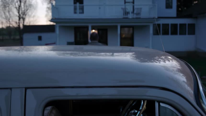 Male grabs his leather satchel then exits a vintage car and proceeds to walk up to the white house through the grass in the front yard