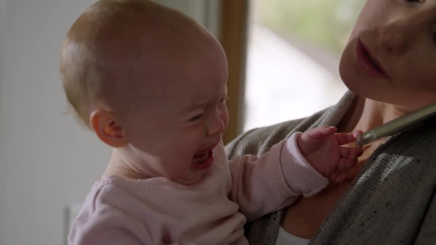 A mother holds her crying baby and soothes her as she talks on the phone
